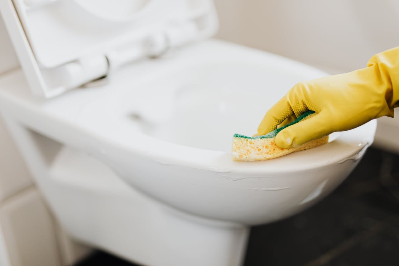 Close-up of a gloved hand using a sponge to clean a toilet, focusing on hygiene.